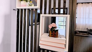 A room with a modern design, featuring a wooden slat partition with two white shelves. One shelf holds a vase with flowers and a picture frame, while the other shelf has a vase with a single flower and a picture frame. - The Home Kololo (Kampala)