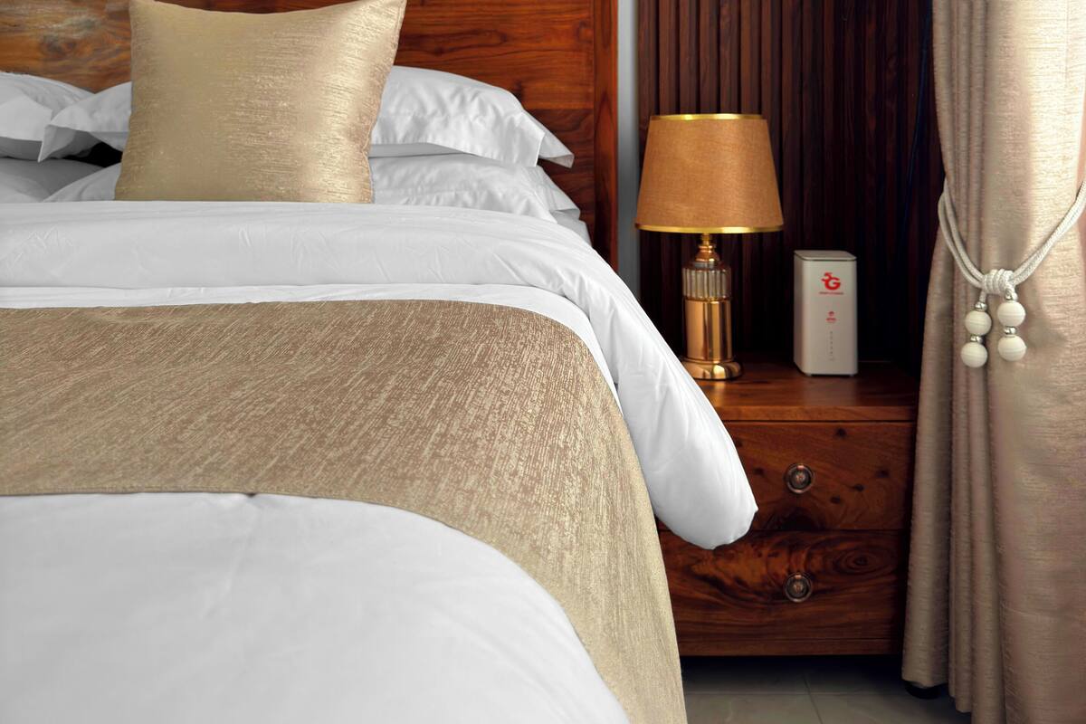 A neatly made bed with a wooden headboard, a bedside table with a lamp, and a framed picture of a landscape on the wall.