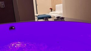A room with a large purple bathtub, a bed with white bedding, and a small table with a vase of flowers. - MAEL SUPERIOR ROOM (Palermo)