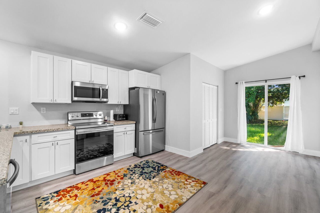 A modern kitchen with white cabinets, stainless steel appliances, and a colorful rug.