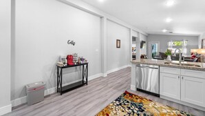 A modern kitchen with white cabinets, a stainless steel dishwasher, and a countertop with a coffee station.