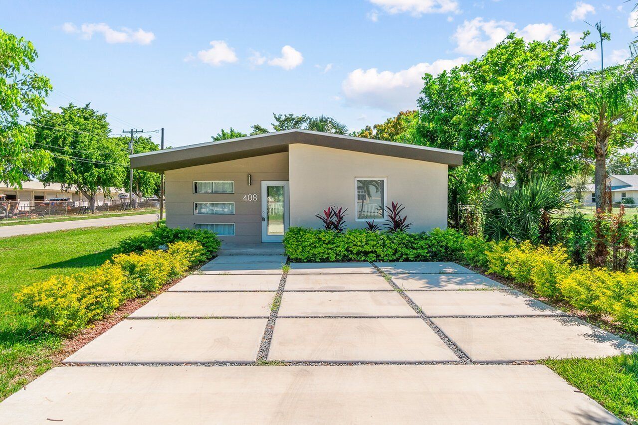 A modern building with a flat roof, numbered 408, surrounded by well-maintained greenery and a clear sky.