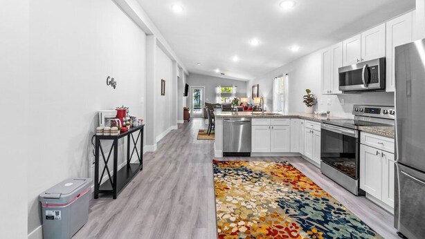 A modern kitchen with white cabinets, stainless steel appliances, and a colorful rug.