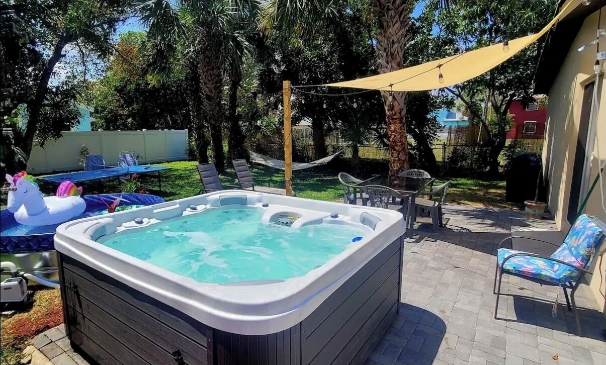 A backyard with a hot tub, lounge chairs, and a hammock.