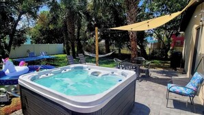 A backyard with a hot tub, lounge chairs, and a hammock.