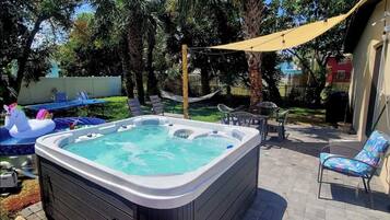 A backyard with a hot tub, lounge chairs, and a hammock.