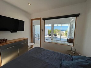 Ein Schlafzimmer mit Bett, einem an der Wand montierten Fernseher, einer Schiebetür zu einem Balkon und Blick ins Freie.