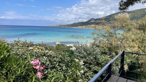 Une vue sur la côte, avec une terrasse en bois donnant sur une plage et des eaux d’un bleu limpide.