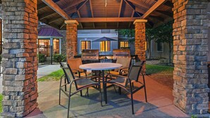 Une terrasse extérieure avec une table ronde et des chaises, un barbecue et des piliers en pierre.