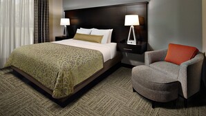 A hotel room with a large bed, two bedside tables with lamps, a grey armchair, and a patterned carpet.