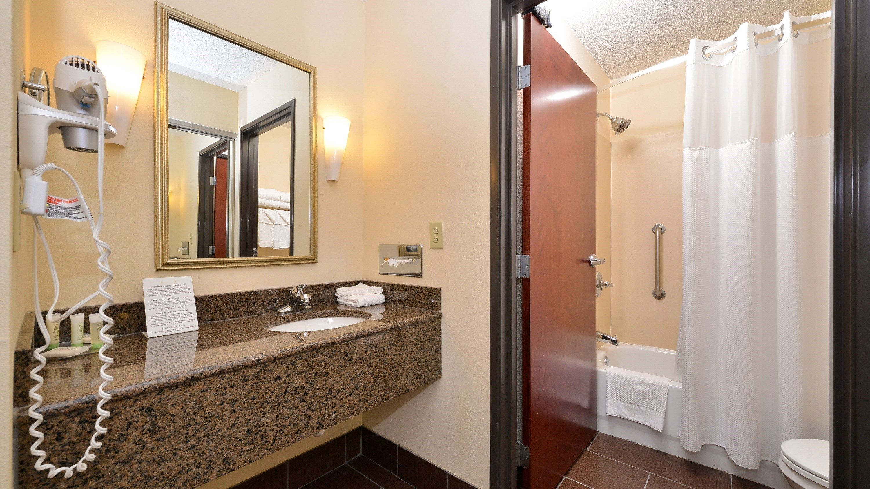 A bathroom with a granite countertop, a sink, a mirror, a hairdryer, and a shower with a curtain.