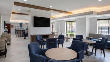 A modern hotel lobby with seating areas, a bar, and a television mounted on the wall.