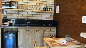Cocina compacta con encimera de madera, un lavamanos y un pequeño comedor con mesa y sillas.