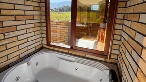 Un jacuzzi en una habitación con paredes de ladrillo y un amplio ventanal corredera a un balcón.