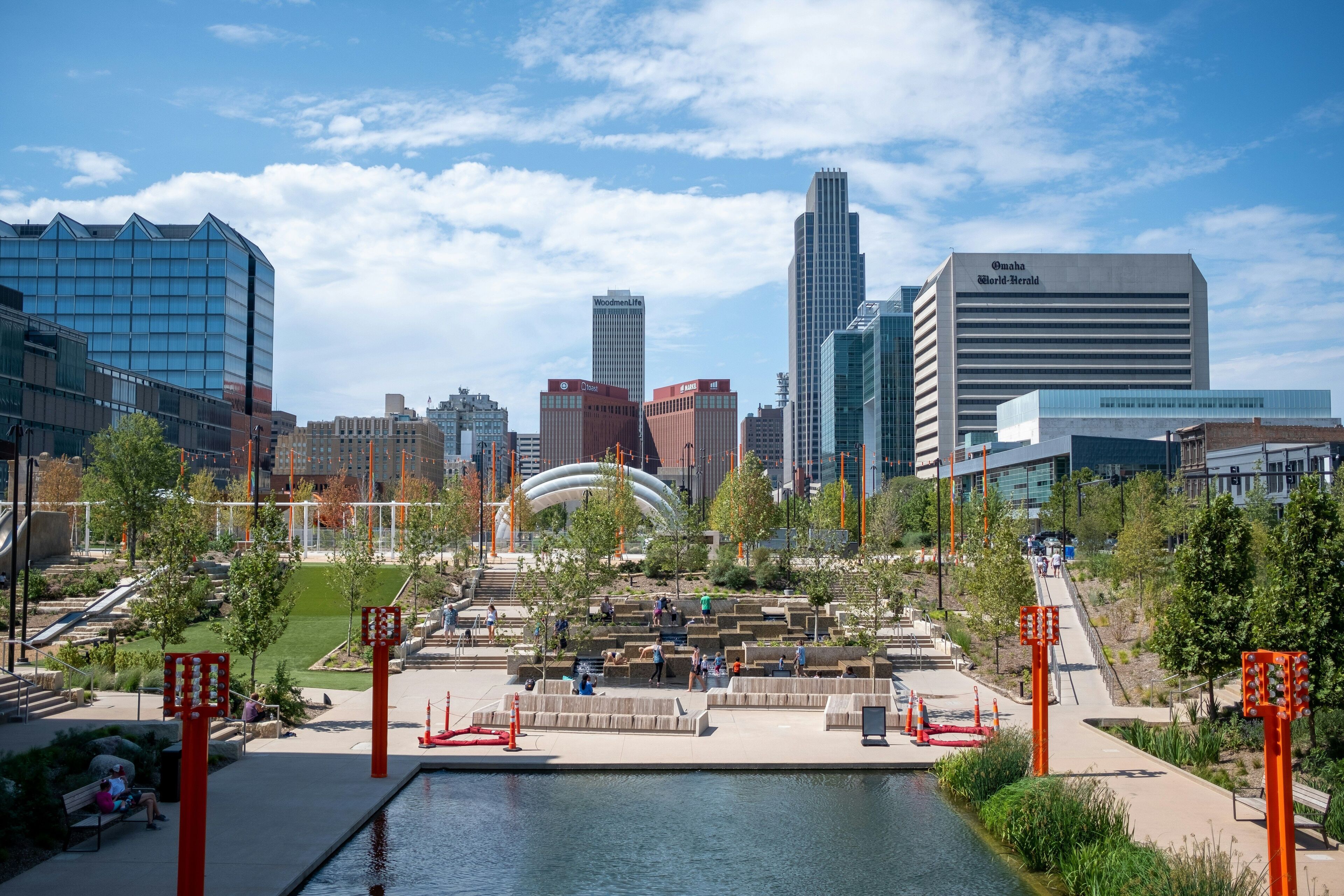 Un paysage urbain avec des bâtiments modernes, un parc central doté de sentiers et une étendue d’eau.