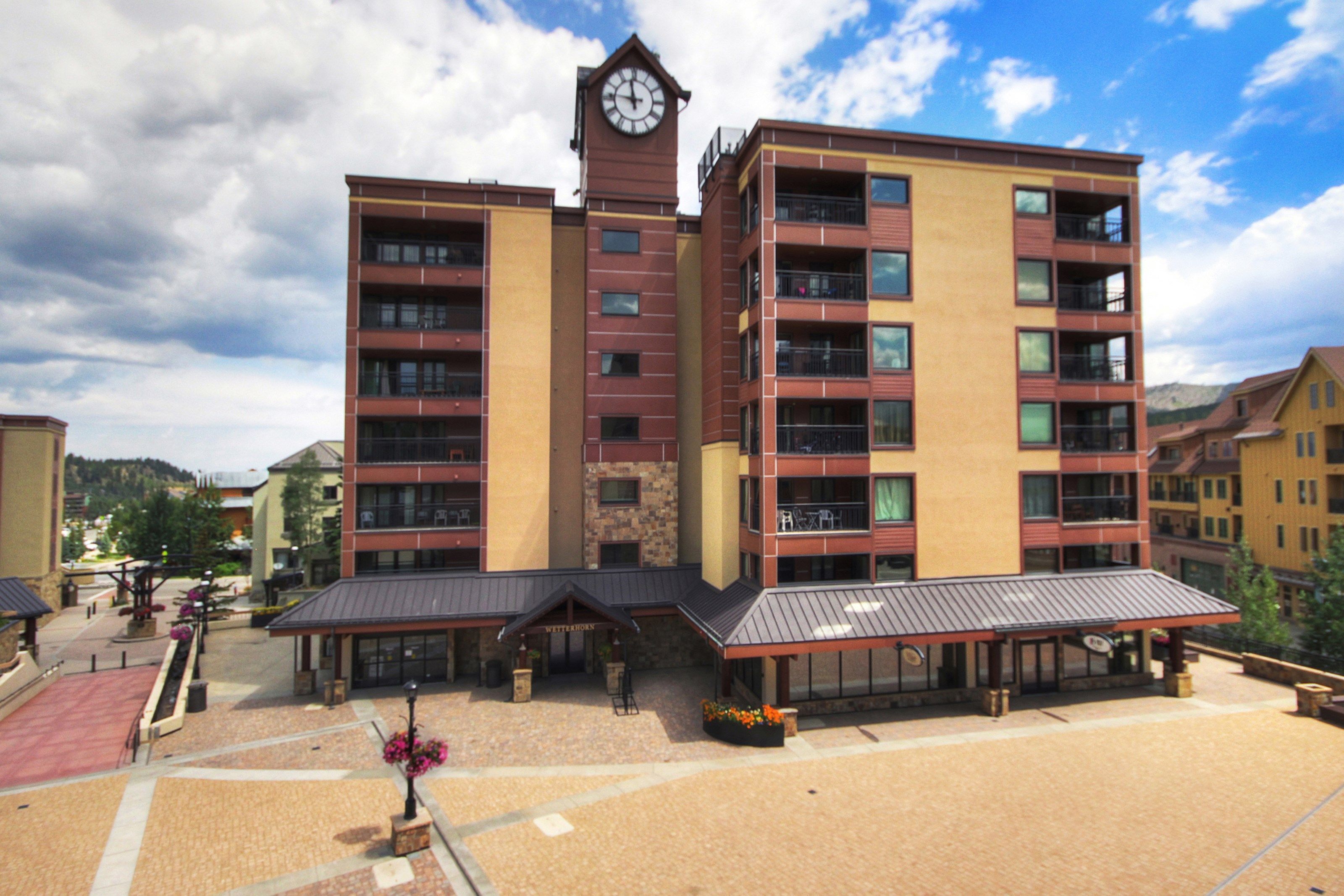 A multi-story hotel with a clock tower, outdoor seating, and a covered patio area.