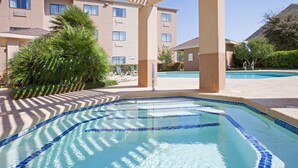 A swimming pool with blue mosaic tiles, surrounded by lounge chairs and palm trees, with a building in the background. - Relaxing Retreat Near Angelo State University! Shared Outdoor Pool (San Angelo)
