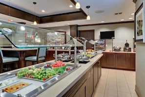 Zona de buffet con diversas frutas y un refrigerador de Coca-Cola.