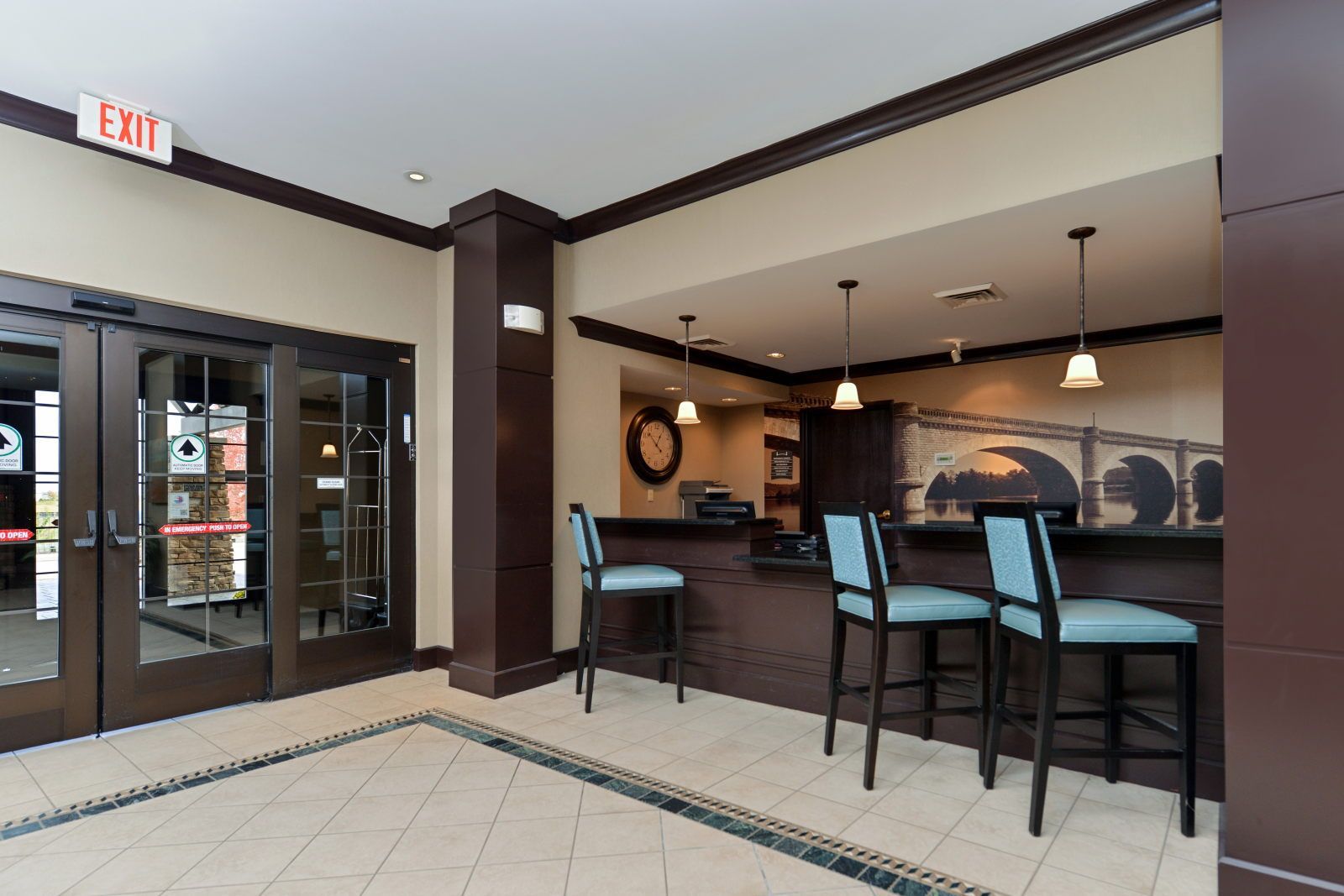 A hotel lobby with an exit sign, a reception desk, and three chairs.