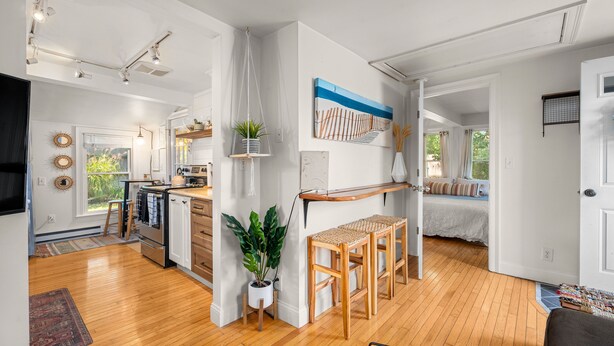 Een ruime woonkamer met houten vloer, een eettafel en een keuken op de achtergrond.