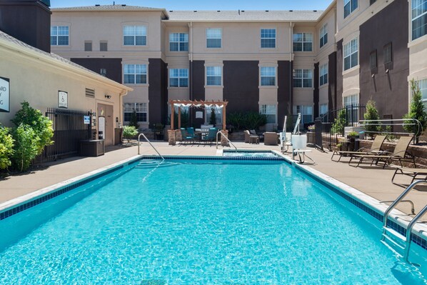 Une piscine avec des chaises longues et une pergola, située dans la cour d’un immeuble à plusieurs étages.