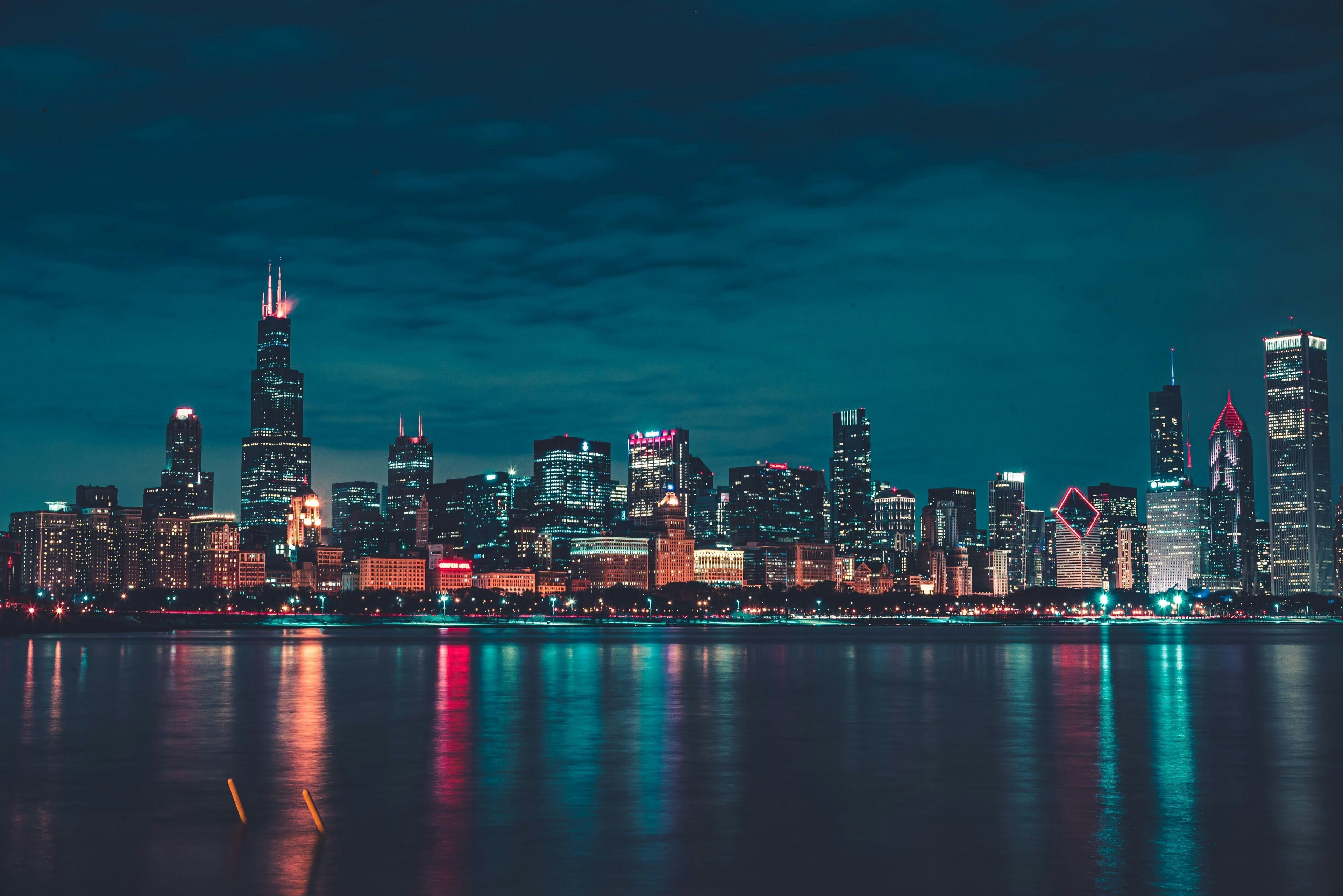 A nighttime city skyline with illuminated buildings reflecting on the water.