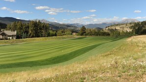 Un parcours de golf doté d’un club-house, entouré de montagnes et d’arbres.