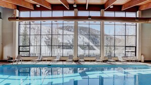 Un espace piscine offrant une vue sur les montagnes enneigées grâce à de grandes fenêtres.