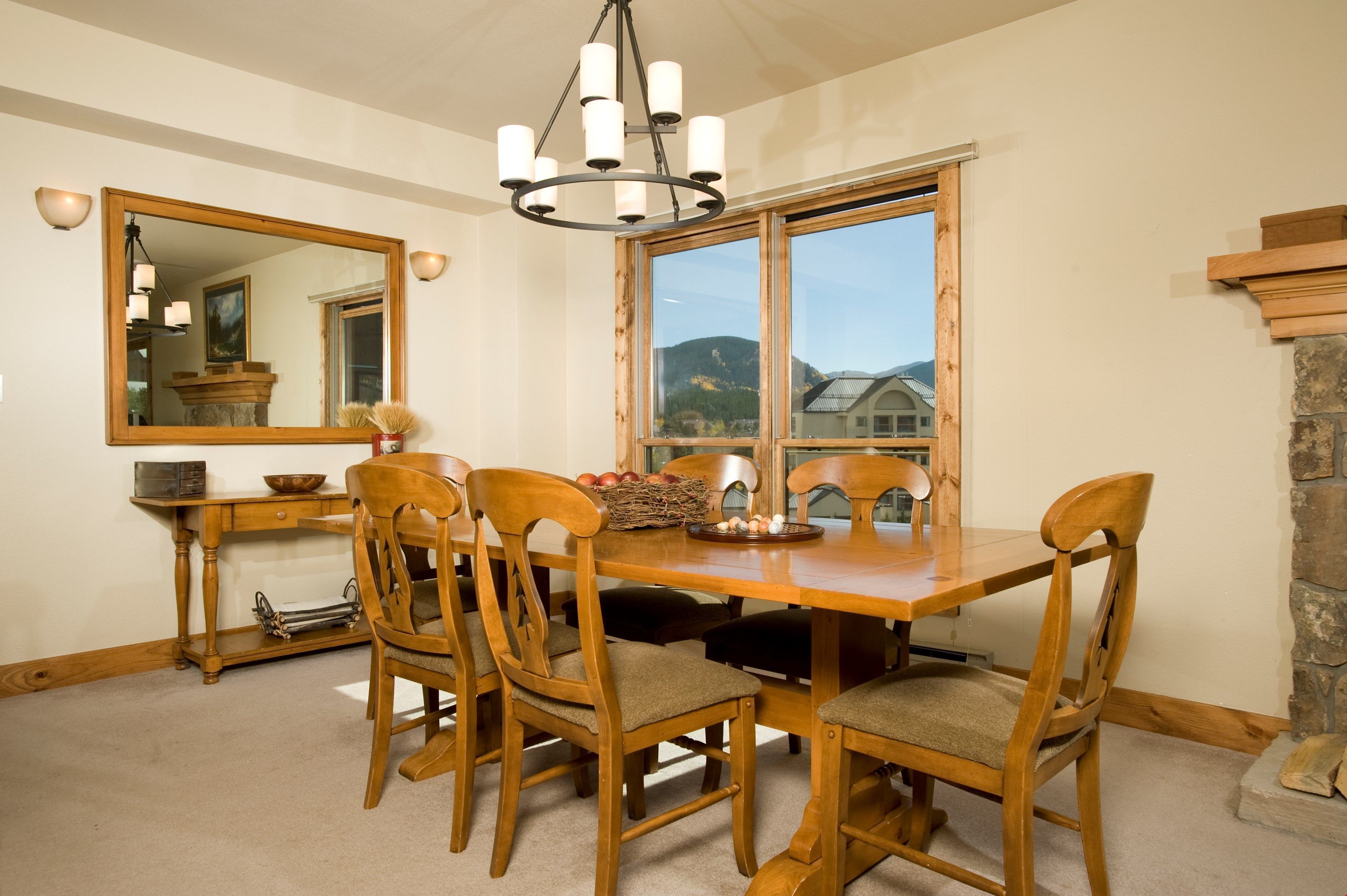 Une salle à manger avec une table et des chaises en bois, un lustre, un grand miroir et une fenêtre donnant sur les montagnes.