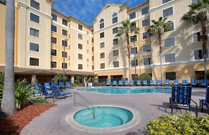 A hotel with a swimming pool, blue lounge chairs, and palm trees. - Cozy Suite | Shared outdoor pool & fitness center (Orlando)