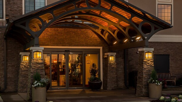 A hotel entrance with a stone facade, a modern arched roof, and outdoor lighting. - Complimentary Breakfast Buffet | Minutes from Shopping + White Sand Beaches (Gulf Shores)