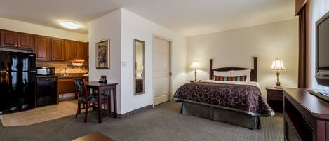 A hotel room with a bed, bedside tables, a desk, a chair, a kitchenette, and a TV.
