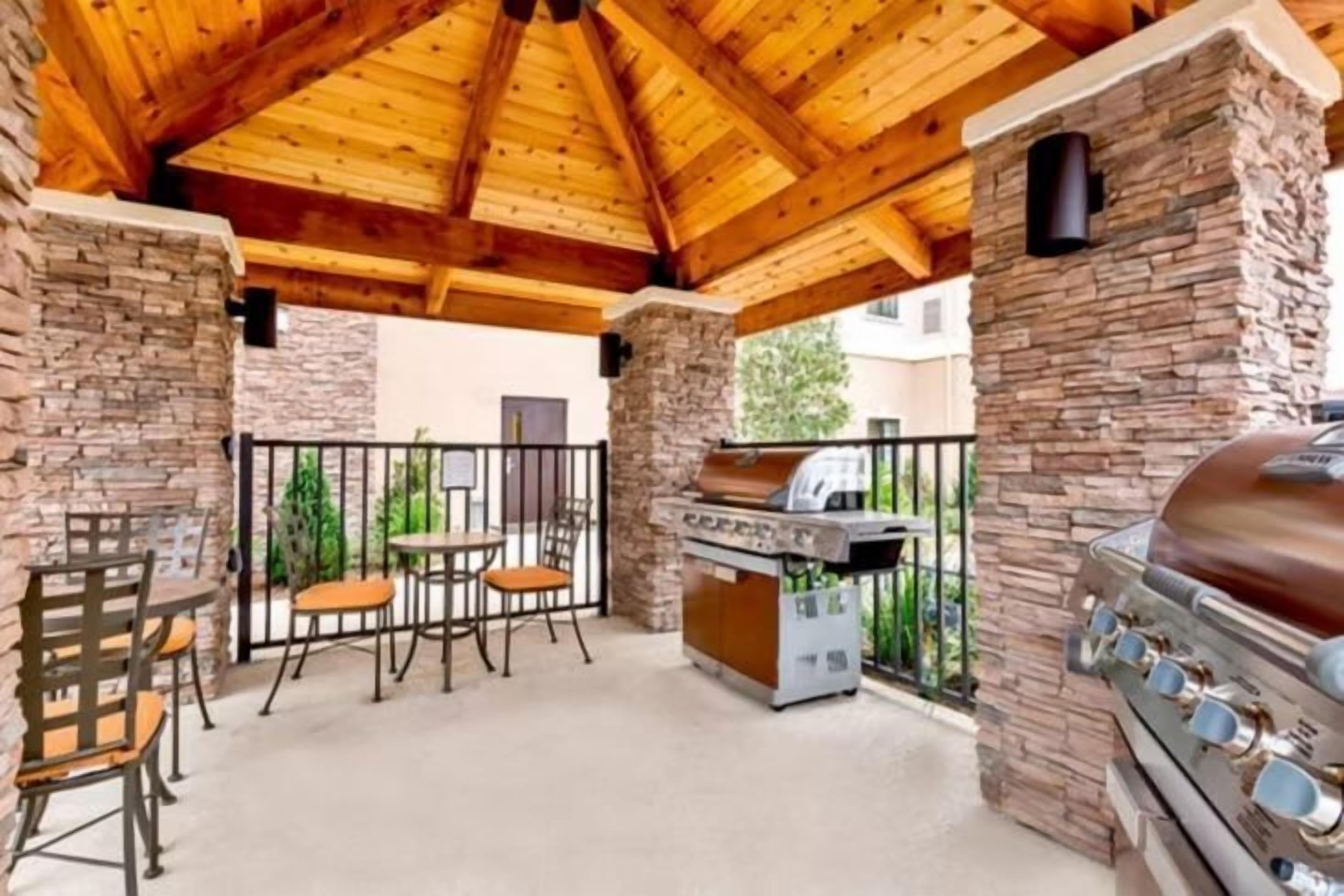 Un patio al aire libre con paredes de piedra, techo de madera y una parrilla para barbacoa.