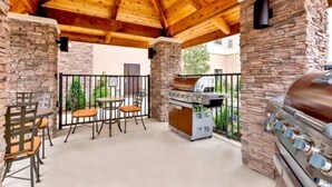 An outdoor patio with stone walls, a wooden ceiling, and a barbecue grill. - Short Drive to Texas A&M | Outdoor Pool + Business Center + Fitness Center (College Station)