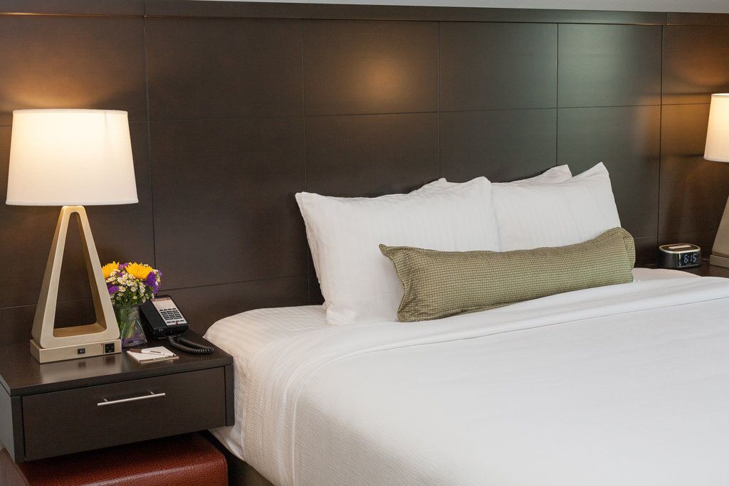 Une chambre d’hôtel avec un grand lit, une table de chevet avec une lampe, un téléphone et un vase rempli de fleurs.