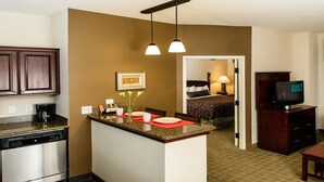 A compact hotel room with a kitchenette, a dining area, a bedroom, and a TV. - Free Breakfast + Outdoor Pool + Hot Tub | Modern Suite (Webster)