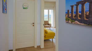 A hallway with a white door marked "Bathroom," a yellow sofa, and a painting of ancient ruins. - Venere Apartment cozy apartment in Sicily overlooking the Mediterranean Sea (Ribera)