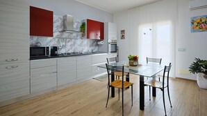 A modern kitchen with a marble backsplash, stainless steel appliances, and a dining area with a glass table and chairs. - Venere Apartment cozy apartment in Sicily overlooking the Mediterranean Sea (Ribera)