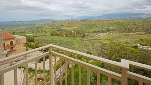 A balcony with a view of a hilly landscape, including fields and distant mountains.