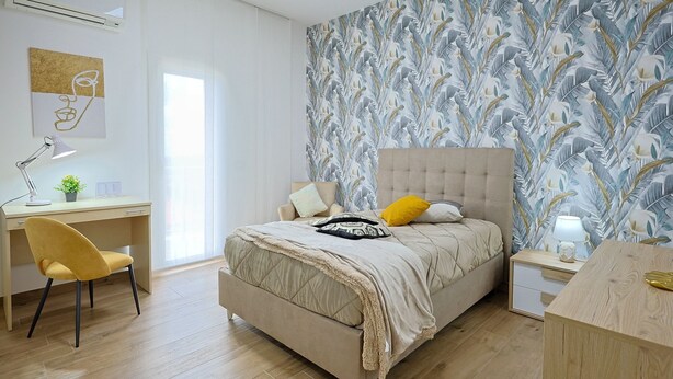A bedroom with a bed, a desk, a chair, and a nightstand.