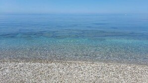 A clear view of a pebble beach leading to calm, shallow waters.
