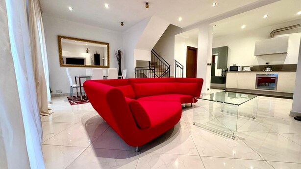 Un vaste espace de vie comprenant un canapé d’angle rouge, une table à manger avec des chaises et un coin cuisine doté d’une table à plateau en verre.