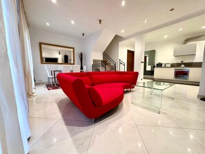 Un vaste espace de vie comprenant un canapé d’angle rouge, une table à manger avec des chaises et un coin cuisine doté d’une table à plateau en verre.