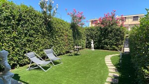 Un jardin bien entretenu, agrémenté de deux chaises longues, d’une statue et d’une haie.