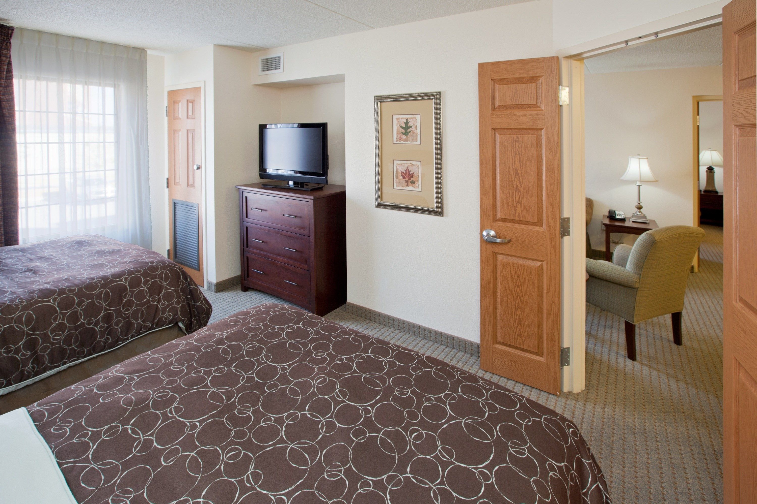 A hotel room with two beds, a TV, a dresser, and a door leading to another room.