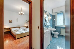 A bedroom with a wooden bed, bedside table, and a nightstand. Adjacent is a bathroom with a sink, mirror, and toilet. - Dora (Riva del Garda)