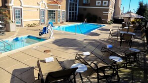 A pool area with lounge chairs and umbrellas, surrounded by a building with balconies and large windows. - Air-Conditioned Studio near Downtown San Jose | FREE Shuttle (Milpitas)