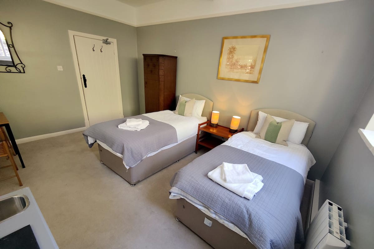 Ein Hotelzimmer mit zwei Betten, einem Nachttisch mit Lampen, einem Kleiderschrank und einem gerahmten Bild an der Wand.
