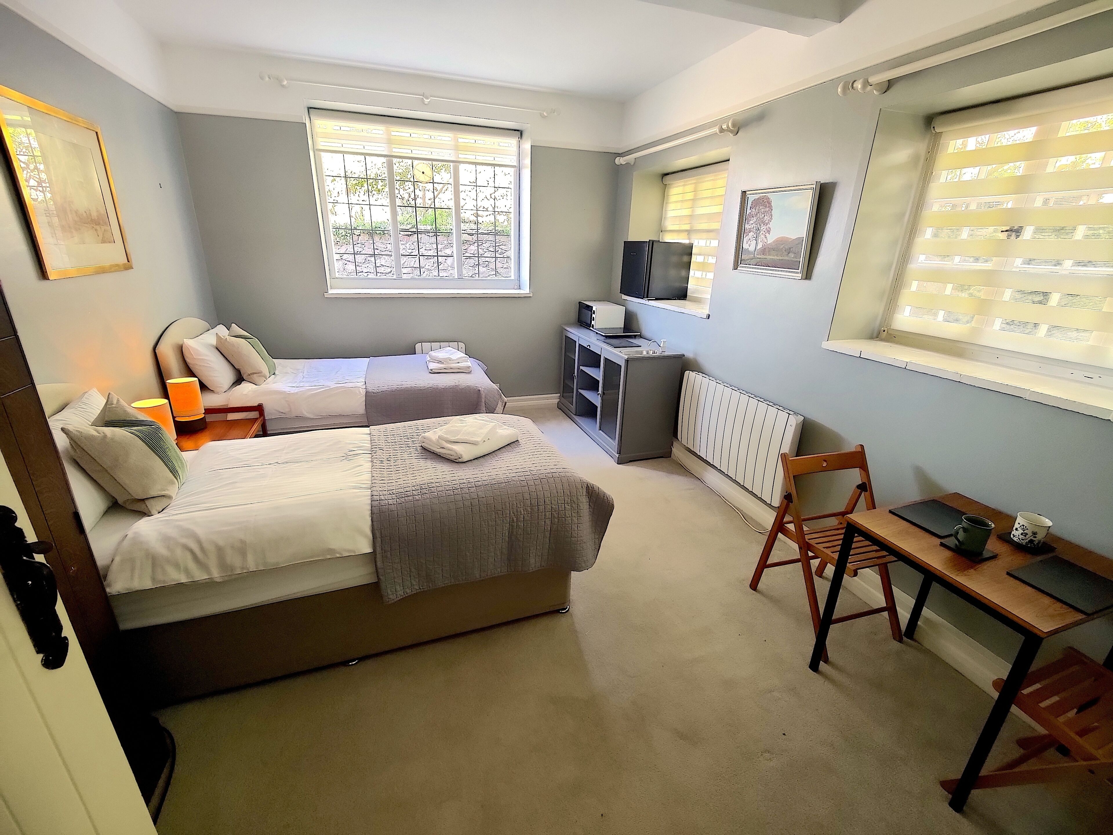 A bedroom with two beds, a desk, a chair, a radiator, and a TV on a shelf.