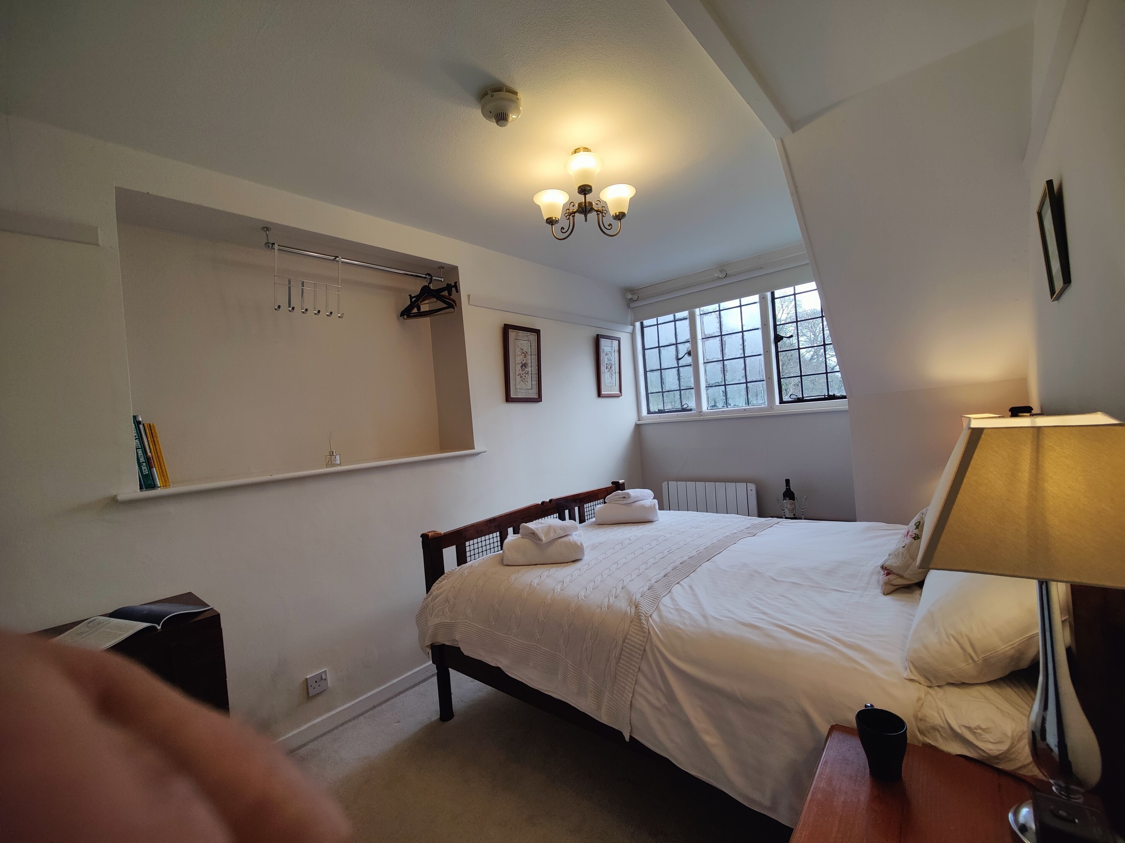 A bedroom with a large bed, a bedside table with a lamp, a radiator, a window with frosted glass, and a ceiling-mounted light fixture.